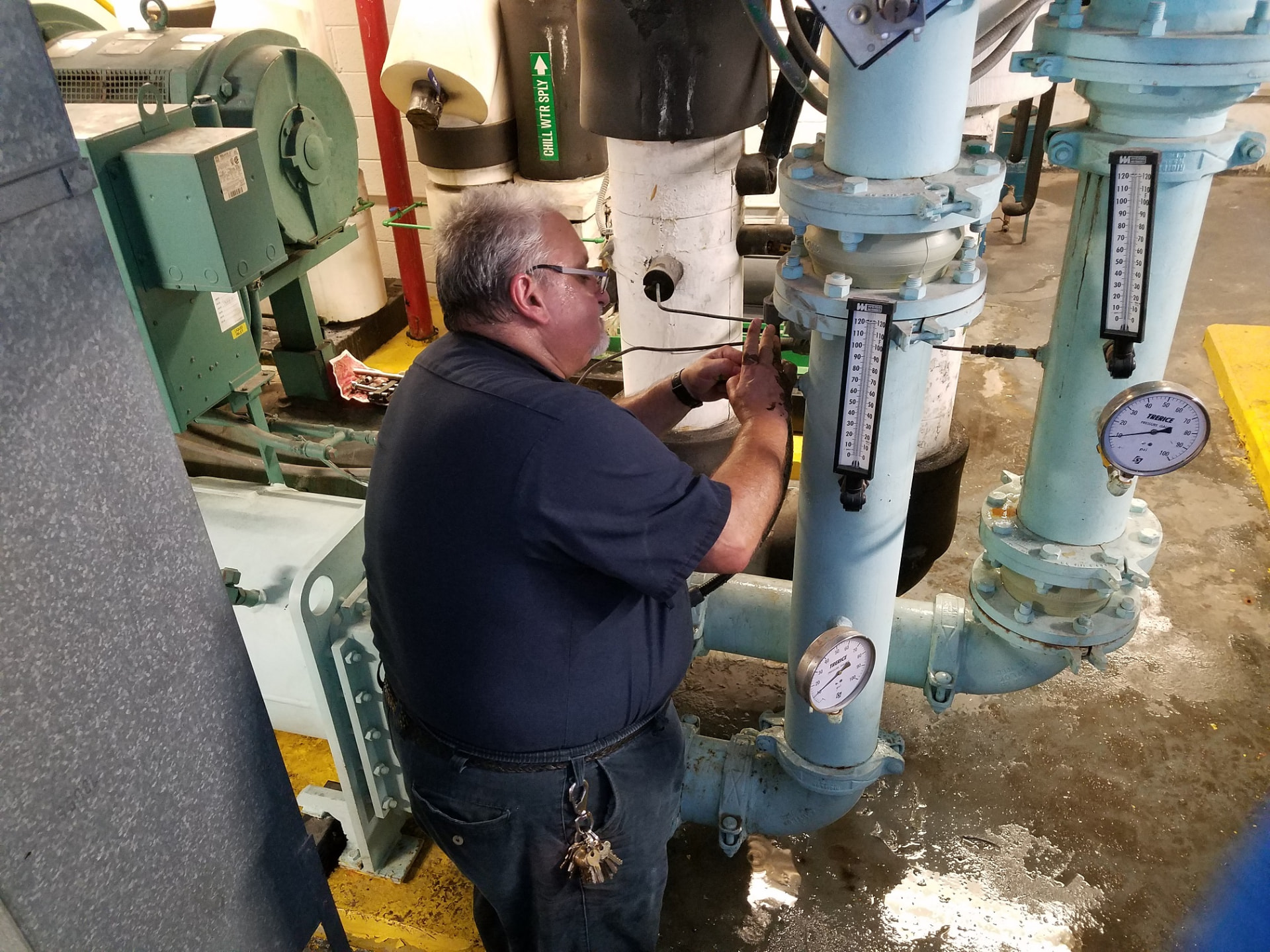 IEI technician servicing chilled water piping and gauges in a mechanical room