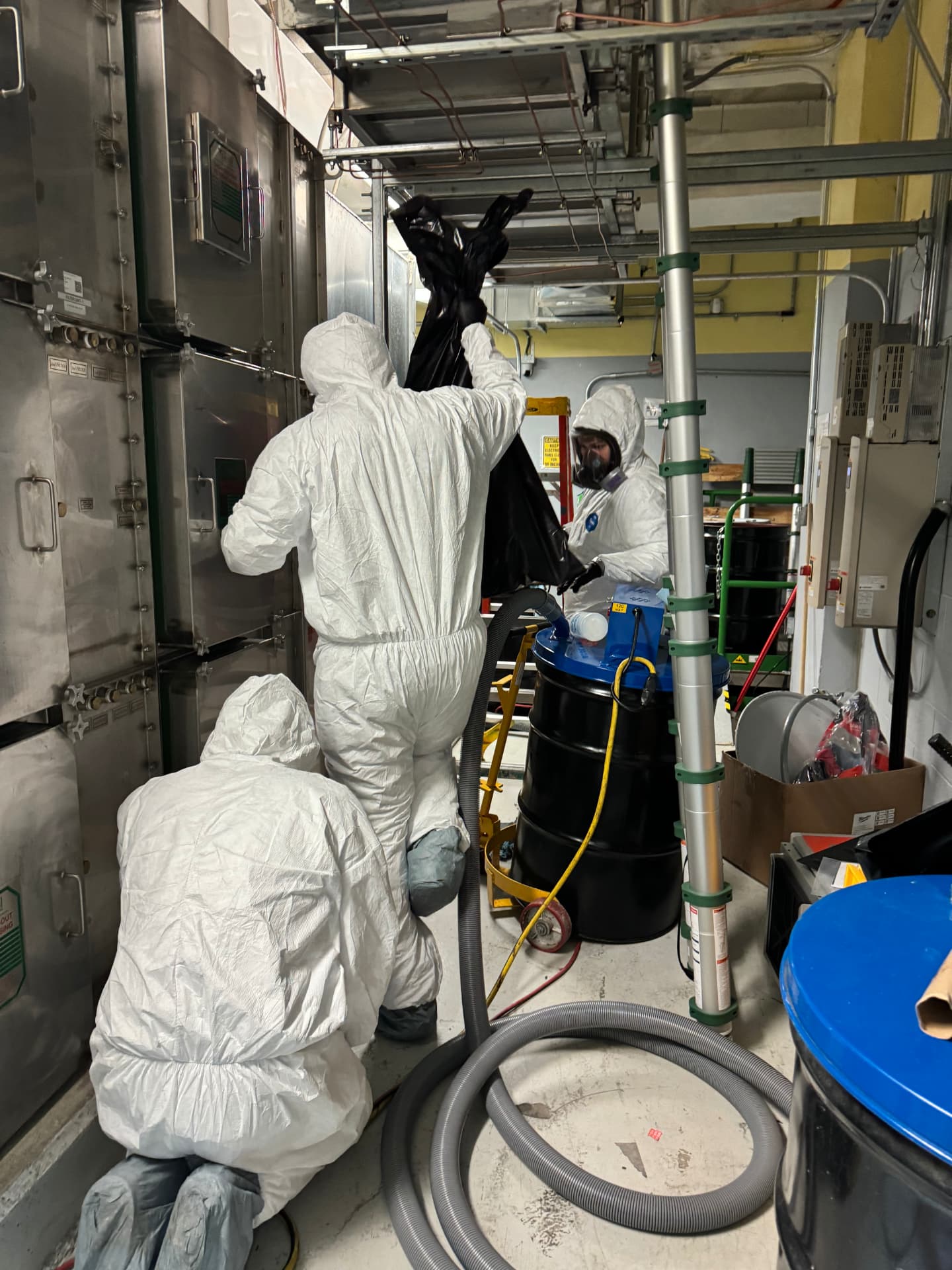 IEI technicians in protective suits and respirators removing hazardous material from a facility mechanical space