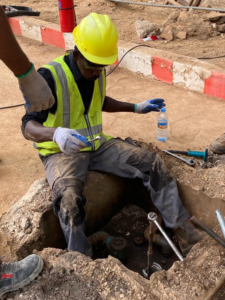 IEI technician in a high-visibility vest and hard hat servicing an underground valve inside an active excavation