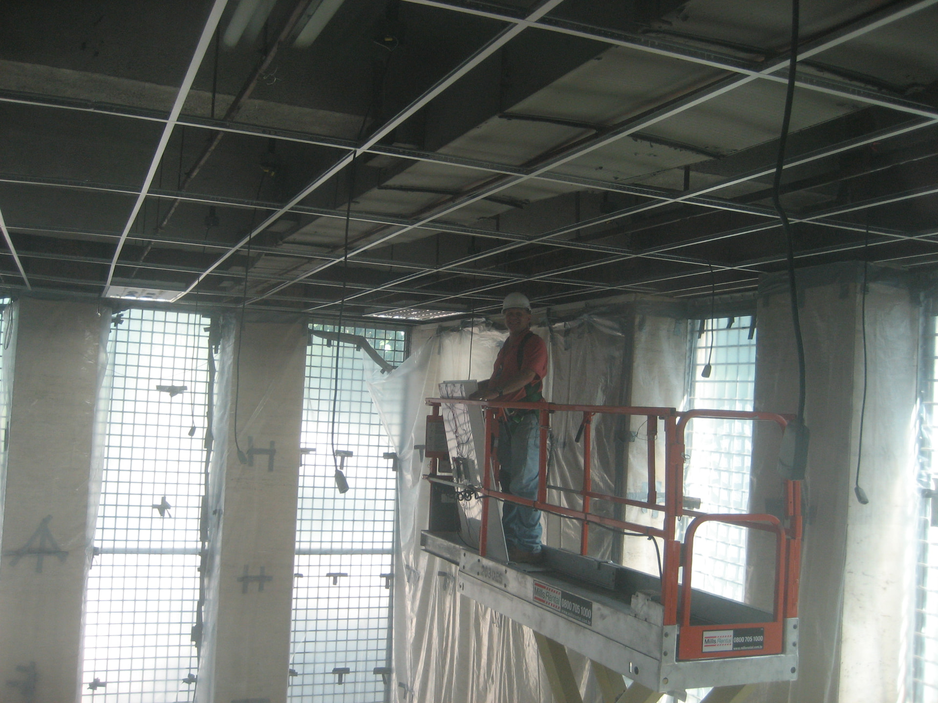 Worker on a scissor lift under plastic containment sheeting during ceiling work in an occupied building